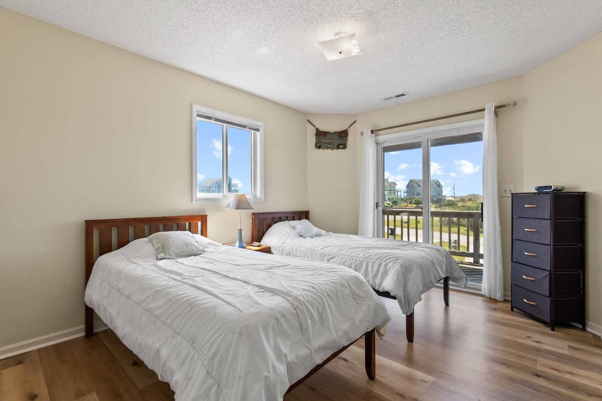 Een slaapkamer met twee bedden, een dressoir en een balkon met uitzicht.