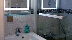 Ein Badezimmer mit weißem Waschbecken, einem Spiegel, einer Dusche und einer gefliesten Wand.
