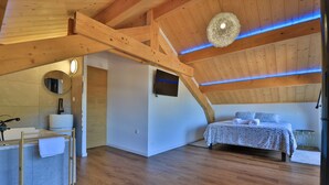 A bedroom with a wooden ceiling, a bed, a bedside table, a mirror, and a window.