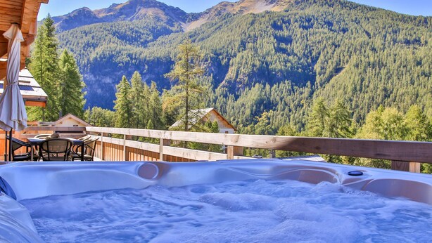 A hot tub with a mountain view, wooden deck, and outdoor seating area.