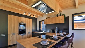 A modern kitchen with wooden cabinetry, a central island with breakfast items, and a large window providing natural light.