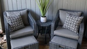 A seating area with two wicker chairs, each with a geometric-patterned pillow, a small round table with a potted plant, and a wall-mounted cow skull decoration. - North Captiva Island- Ocean bay views and modern decor. Two new carts! (Captiva)