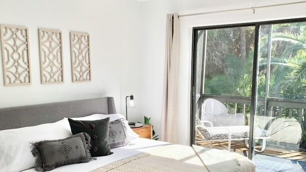A bedroom with a bed, a ceiling fan, a window with a view of greenery, and a sliding glass door leading to an outdoor area. - North Captiva Island- Ocean bay views and modern decor. Two new carts! (Captiva)