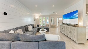 A modern living room with a grey sectional sofa, a white coffee table, and a large flat-screen TV on a white cabinet. - North Shore Very Walkable to Ami fun (Anna Maria)