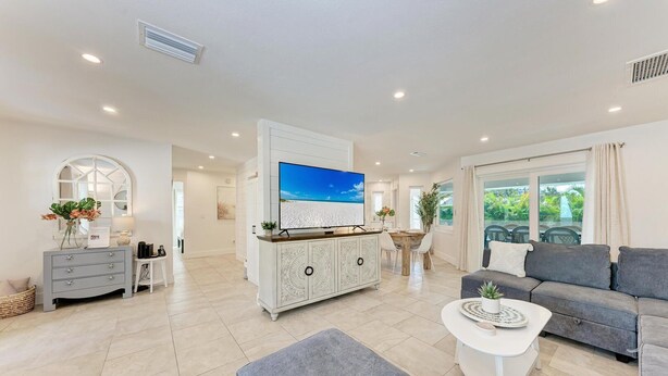 A spacious living area with a large flat-screen TV, a grey sofa, a white coffee table, and a dining area with a wooden table and chairs. - North Shore Very Walkable to Ami fun (Anna Maria)