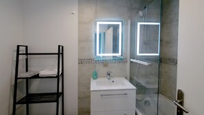 A bathroom with a white sink, a glass shower enclosure, and a black metal shelf unit. - T2 Orly center ville Close to Paris and shops (Orly)
