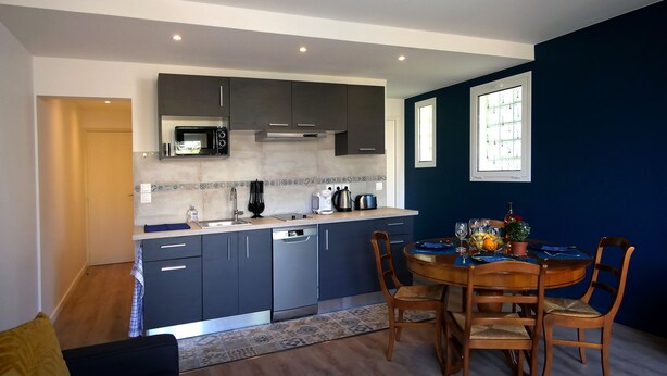 A modern kitchen with dark cabinets, a microwave, and a coffee maker. There is a dining table with chairs and a window with blinds. - T2 Orly center ville Close to Paris and shops (Orly)