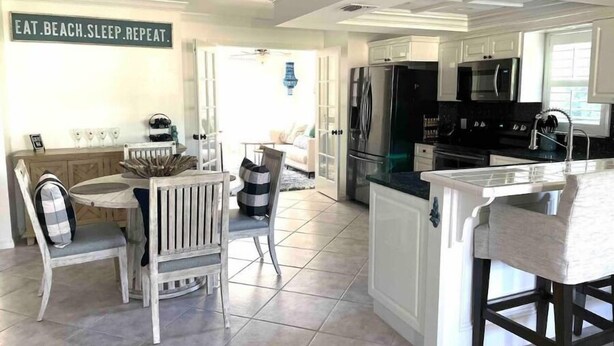 Une cuisine moderne avec des meubles blancs, un îlot central et un coin repas comprenant une table et des chaises blanches.