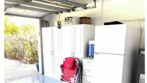 Un garage avec un réfrigérateur blanc, une valise rouge et un projecteur fixé au plafond.