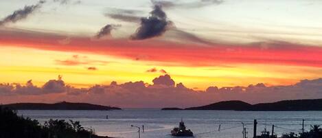 A sunset over a body of water with a ship in the distance and buildings along the shore.