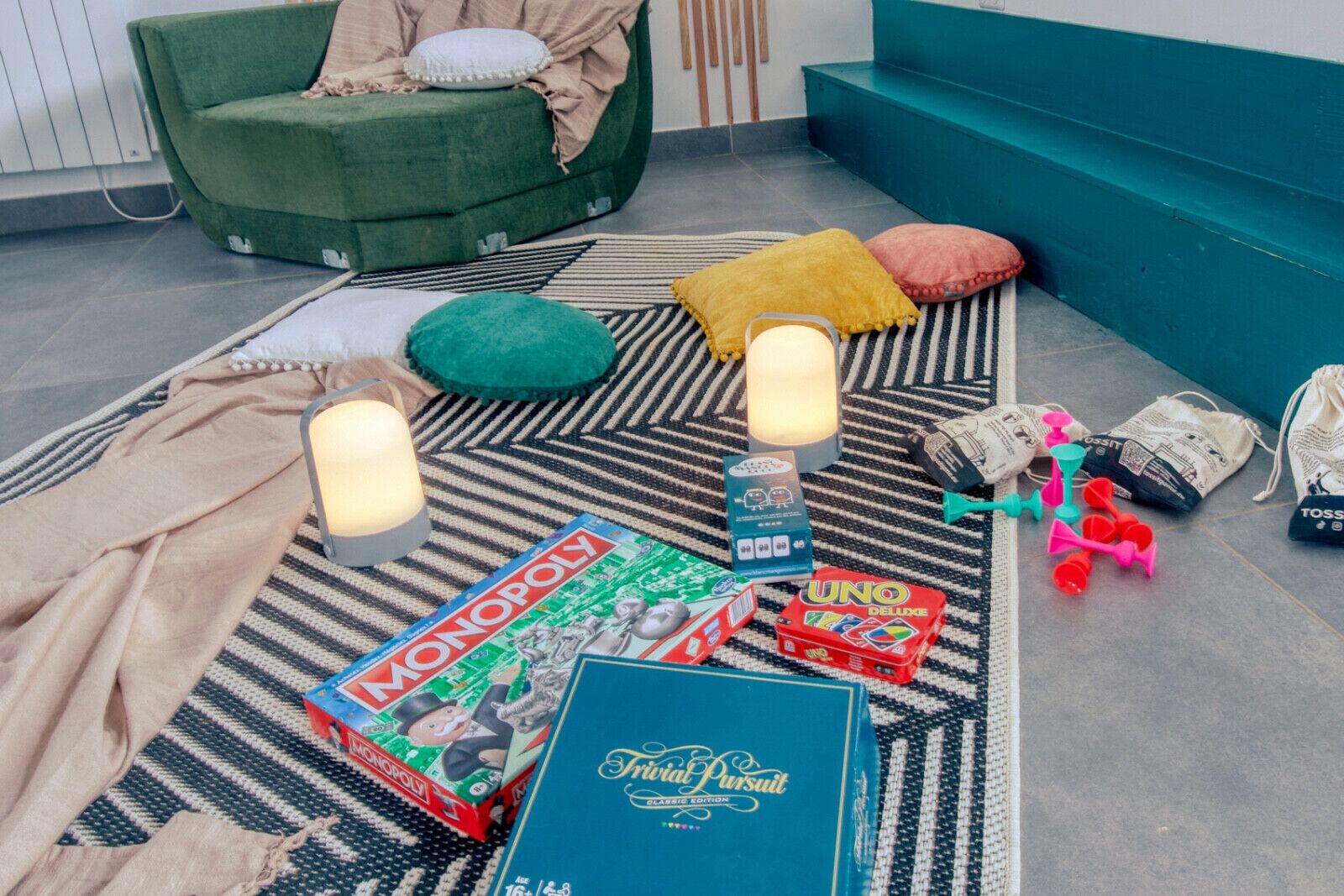 A cozy indoor setting with a green sofa, striped rug, Monopoly board game, and a blue box labeled "Trivial Pursuit."