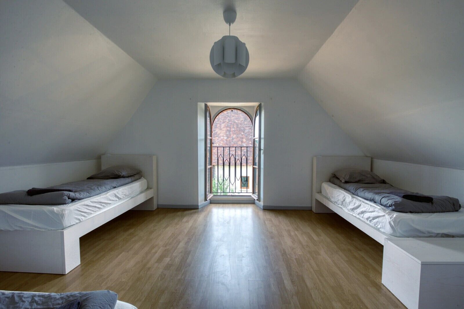 Una habitación con dos camas, piso de madera y tragaluz.