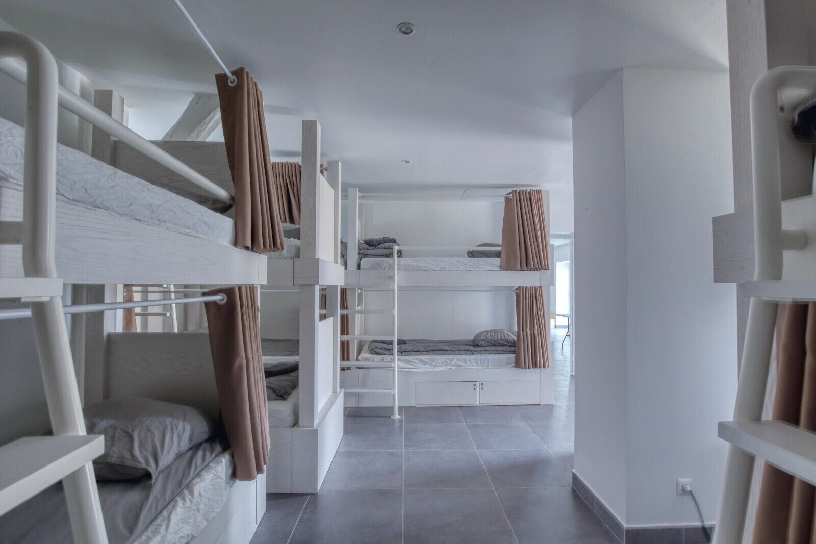 Habitación con literas modernas de varios niveles y un diseño minimalista, con paredes blancas y suelo de baldosas.