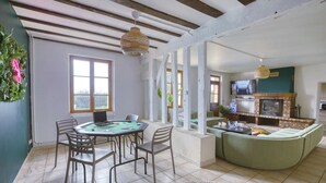 A spacious living area with a round table and chairs, a green sofa, a fireplace, and a television. - So Villa Buisson (41) - Heated swimming pool - Volleyball - 2h from Paris- 30p. (Couëtron-au-Perche)