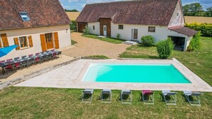 A pool area with lounge chairs, a dining setup, and a building with a tiled roof. - So Villa Buisson (41) - Heated swimming pool - Volleyball - 2h from Paris- 30p. (Couëtron-au-Perche)