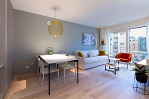 Una sala de estar moderna con un sofá blanco, una mesa de comedor con sillas, un sillón rojo y un ventanal con vistas a la ciudad.
