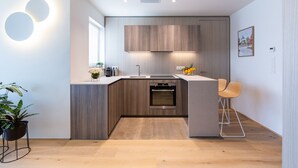 Eine moderne Küche mit Holzschränken, einem Einbauofen und einer kleinen Essecke mit einem Barhocker.