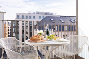 Un balcón con una mesa dispuesta para una comida, que incluye pan, queso, uvas y una botella.