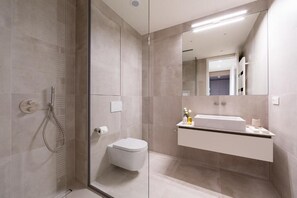 Un baño moderno con cabina de ducha de vidrio, inodoro blanco y tocador empotrado con espejo.