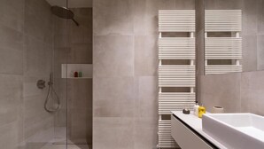 A modern bathroom with a glass shower enclosure, a white bathtub, and a built-in towel rack. - Deluxe Studio      . (Luxembourg)