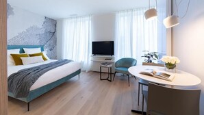 A modern hotel room with a bed, a TV, a small table with a chair, and a window with curtains. - Deluxe Studio      . (Luxembourg)