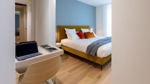 Una habitación de hotel moderna con una cama de madera, un escritorio con una computadora portátil y una pared azul decorativa.