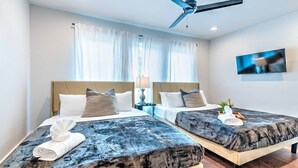 Ein Hotelzimmer mit zwei Betten, einem Deckenventilator, einem Fernseher und einem Fenster mit Vorhängen.