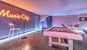 Une table de billard dans une pièce où l’on peut voir un panneau au néon indiquant « Music City » et une cible de fléchettes accrochée au mur.