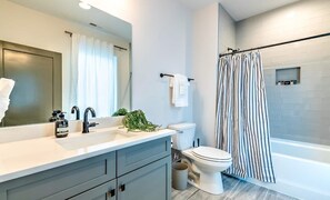 A modern bathroom with a large mirror, a sink with soap dispensers, a toilet, and a shower with a striped curtain.