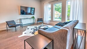 Ein modernes Wohnzimmer mit einer Couch, zwei Sesseln, einem Couchtisch und einem an der Wand montierten Fernseher.