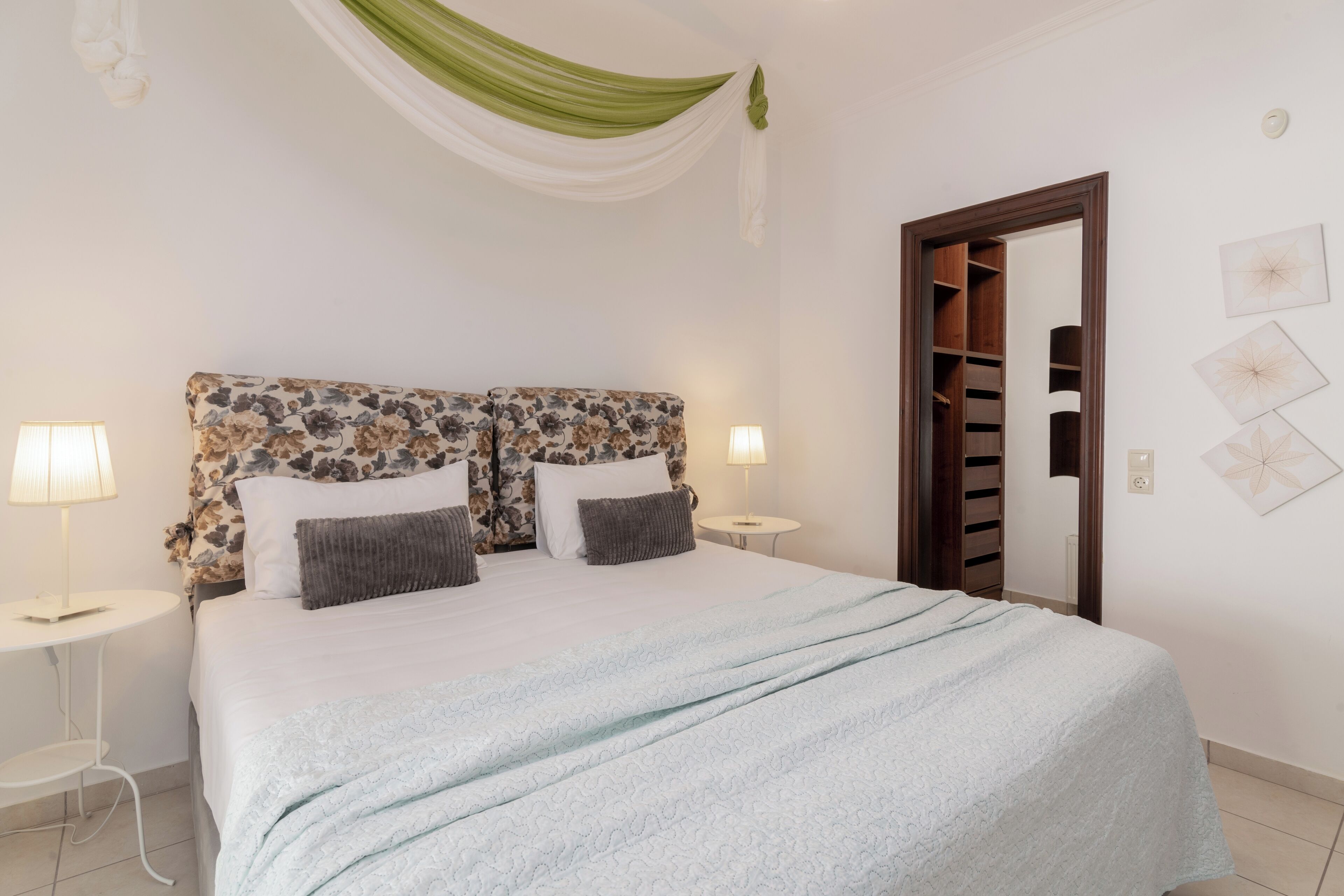 Een netjes opgemaakt slaapkamer met een bloemen hoofdbord, twee bedlampen, een lichtblauwe sprei en een houten garderobe.