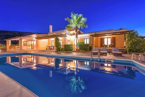 Una casa lujosa con piscina, mobiliario exterior y un patio bien iluminado.