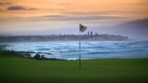 A golf course with a flagstick in the foreground and a coastal cityscape in the background. - Luxury Townhouse in the centre of St Andrews (St Andrews)