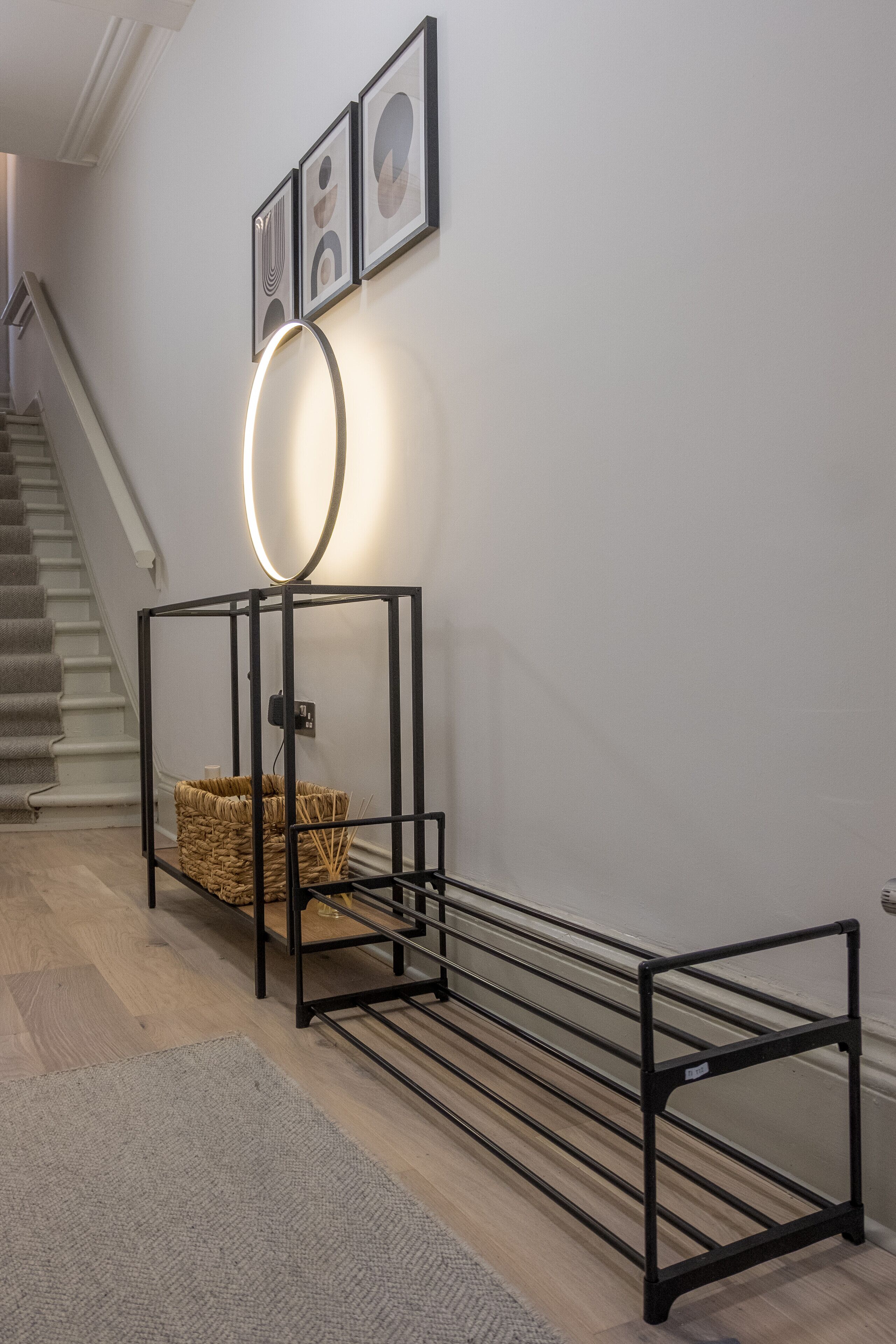 A hallway with a black metal rack, a woven basket, and framed pictures on the wall.