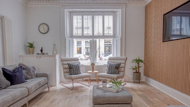 A modern living room with a sofa, two armchairs, a coffee table, and a large window with shutters. - Luxury Townhouse in the centre of St Andrews (St Andrews)