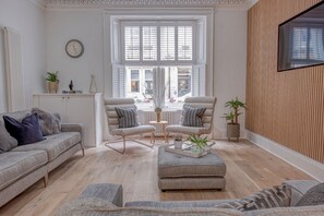 A modern living room with a sofa, two armchairs, a coffee table, and a large window with shutters.