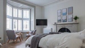 A bedroom with a large bed, a fireplace, a TV, and a window with blinds. - Luxury Townhouse in the centre of St Andrews (St Andrews)