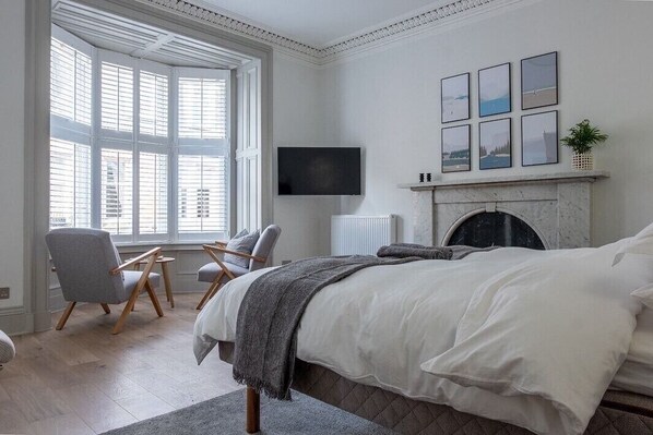 A bedroom with a large bed, a fireplace, a TV, and a window with blinds.