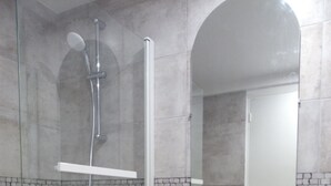 Un baño con ducha de vidrio, banca de madera y espejo en la pared.