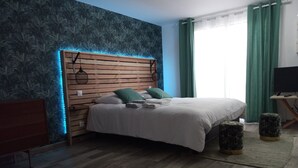 Un dormitorio con cama, cabecero de madera, cortinas verdes y un televisor sobre un mueble.