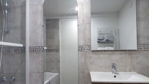 Un baño moderno con ducha acristalada, lavamanos blanco y tocador de madera.