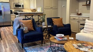 Un salon moderne avec des fauteuils bleus, une table basse et une cuisine en arrière-plan.