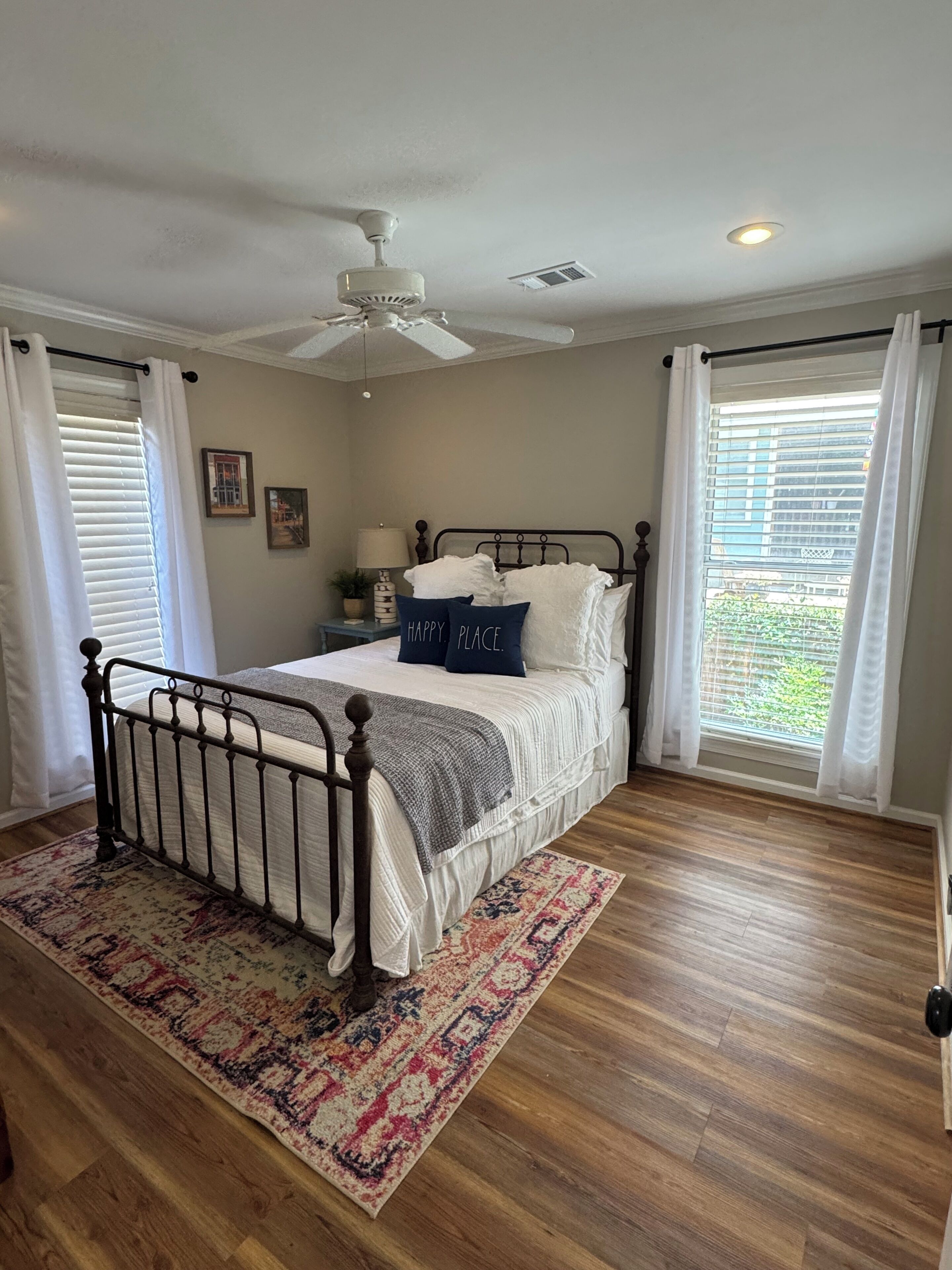 A bedroom with a bed, a ceiling fan, a nightstand, a lamp, and a window with blinds.