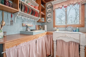 Enjoy cooking in this charming kitchen with a sink and countertop, surrounded by wooden shelves and a collection of dishes.