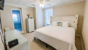 A bedroom with a bed, a desk, a dresser, and a ceiling fan. - Castaway Cottage (Eclectic)