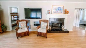 A living room with two wicker armchairs, a flat-screen TV, a fireplace, and a framed picture above it. - Castaway Cottage (Eclectic)
