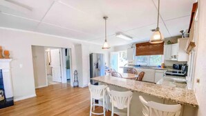 A spacious kitchen with a granite countertop, white chairs, and pendant lighting. - Castaway Cottage (Eclectic)