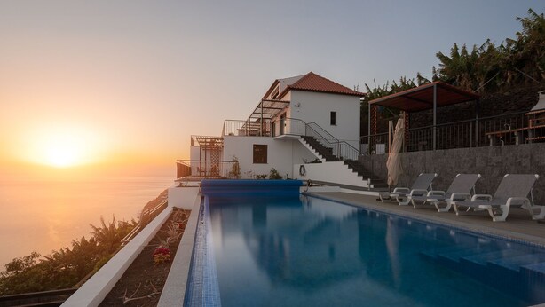Una piscina con vista sul tramonto, un edificio con tetto rosso e una scala che conduce a un balcone.