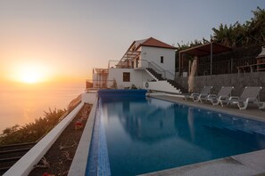 A swimming pool with a view of the sunset, a building with a red roof, and a staircase leading to a balcony. - Nearer to the Sea than the sky, an amazing views and peaceful escape. (Arco da Calheta)