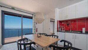 Una cucina moderna con mobili bianchi, uno schienale rosso e vista mare attraverso ampie finestre.